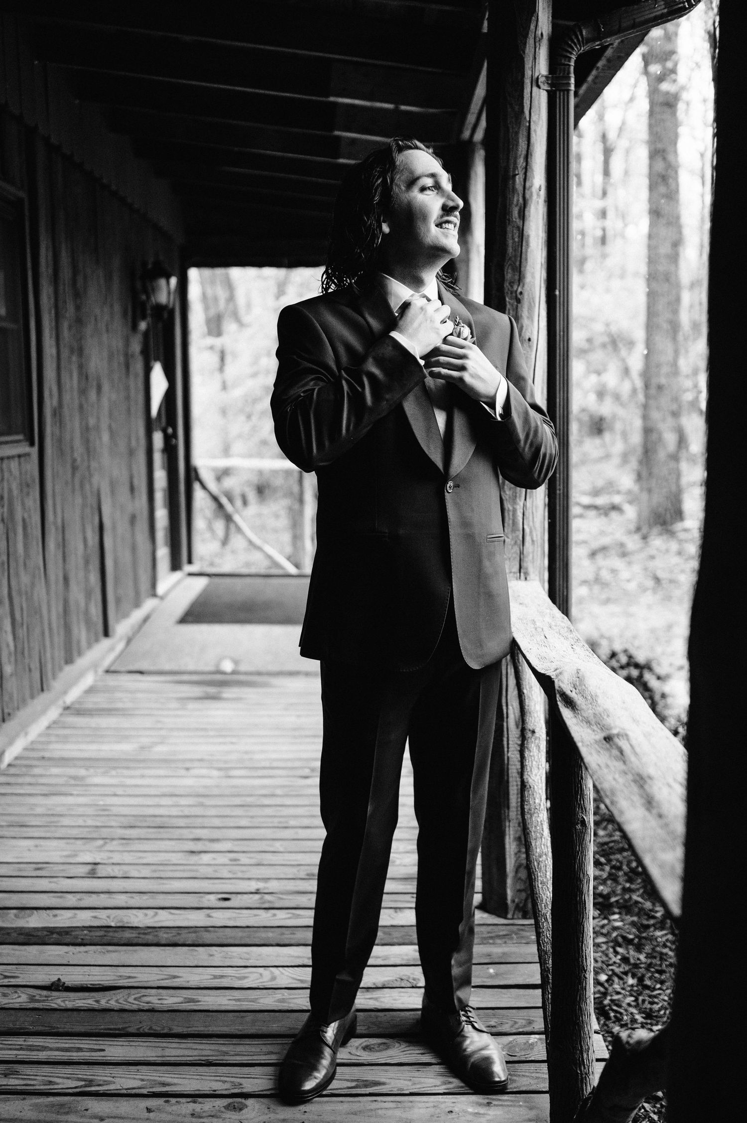 Black and white portrait of someone in a suit expressing joy on a wooden porch.
