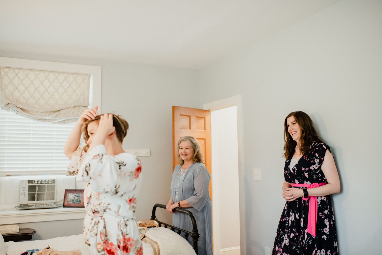Wedding preparation scene in bright bedroom with multiple people getting ready.