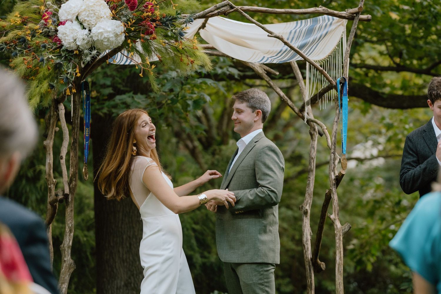 Couple sharing a moment during their ceremony under a flower-adorned wooden arch.