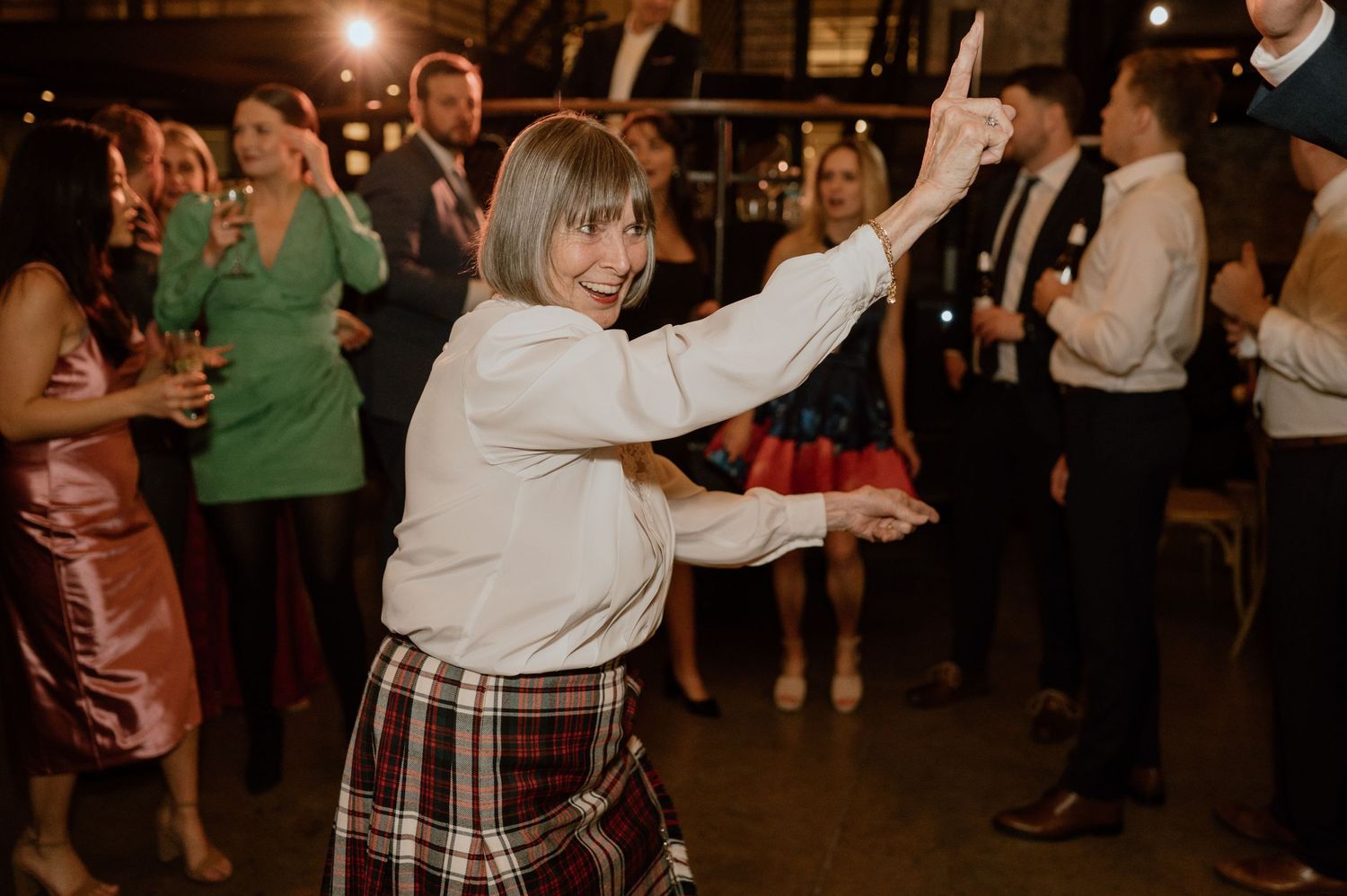 A person in a white sweater and plaid skirt dances energetically at an indoor party.