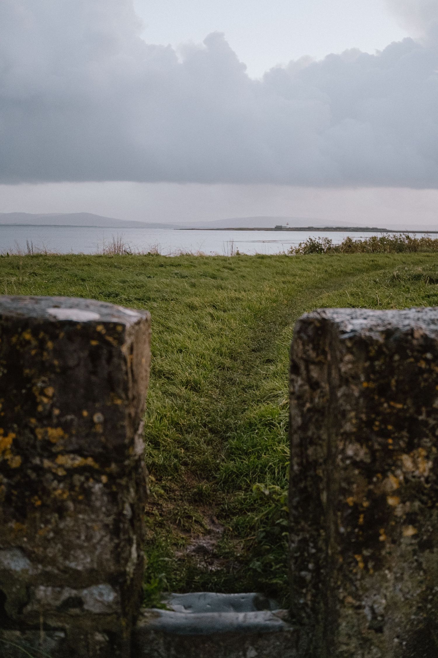 Ancient stone pillars frame a misty coastal landscape view.