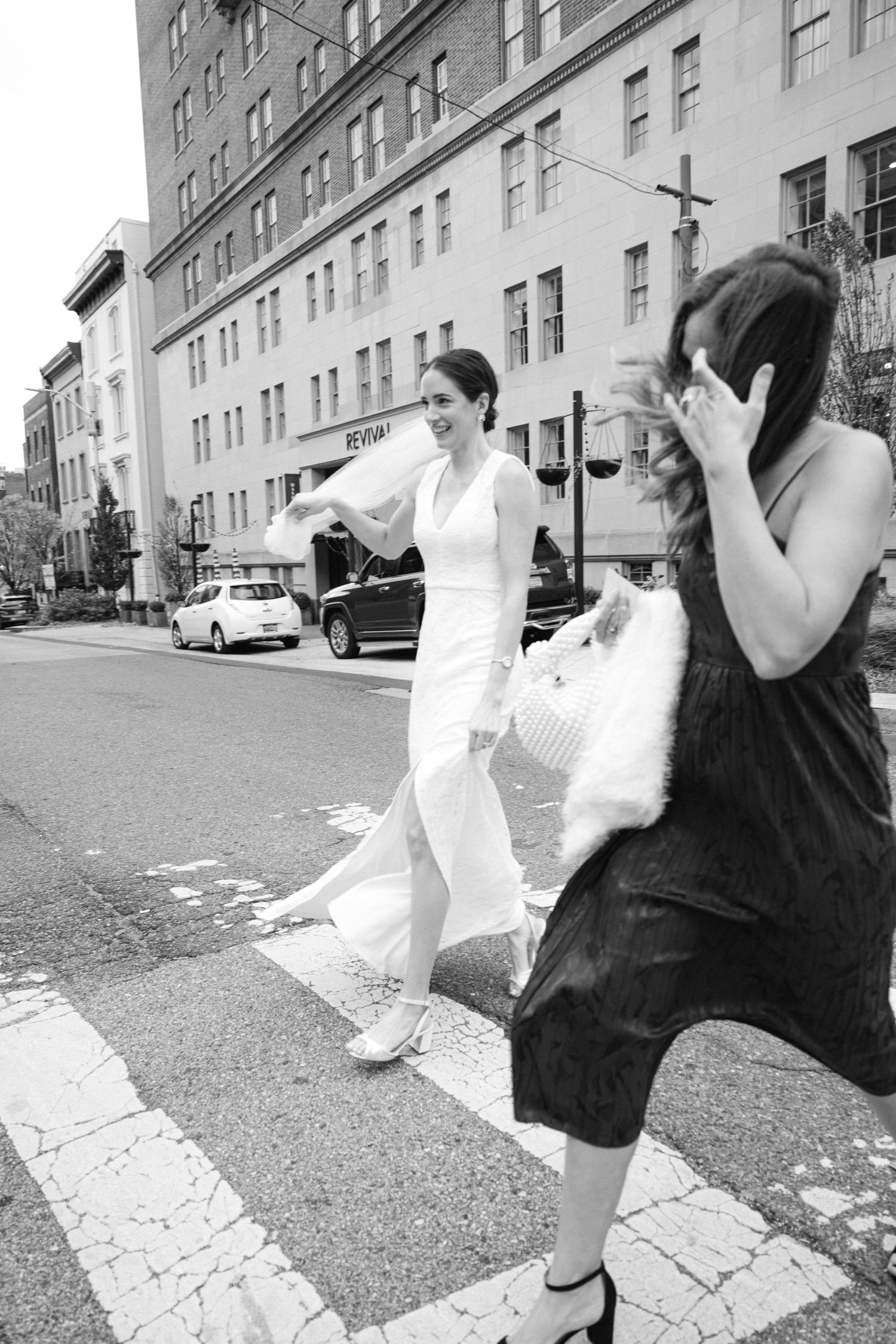 A black and white street scene with a figure in white dress crossing an urban intersection.