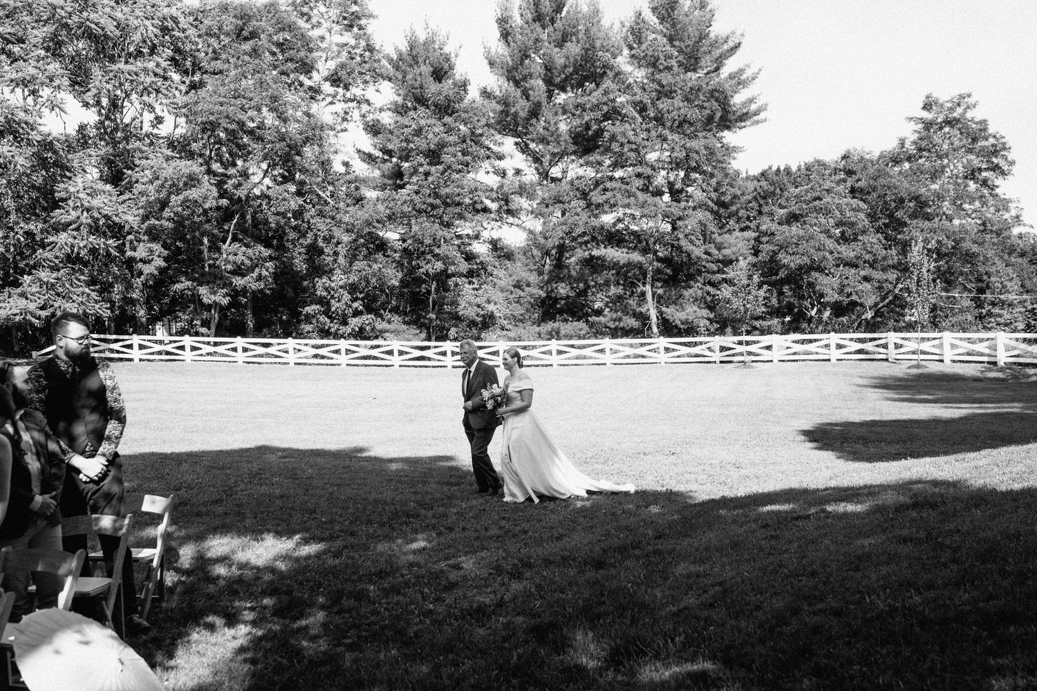Black and white photo of outdoor wedding ceremony with guests seated on lawn.