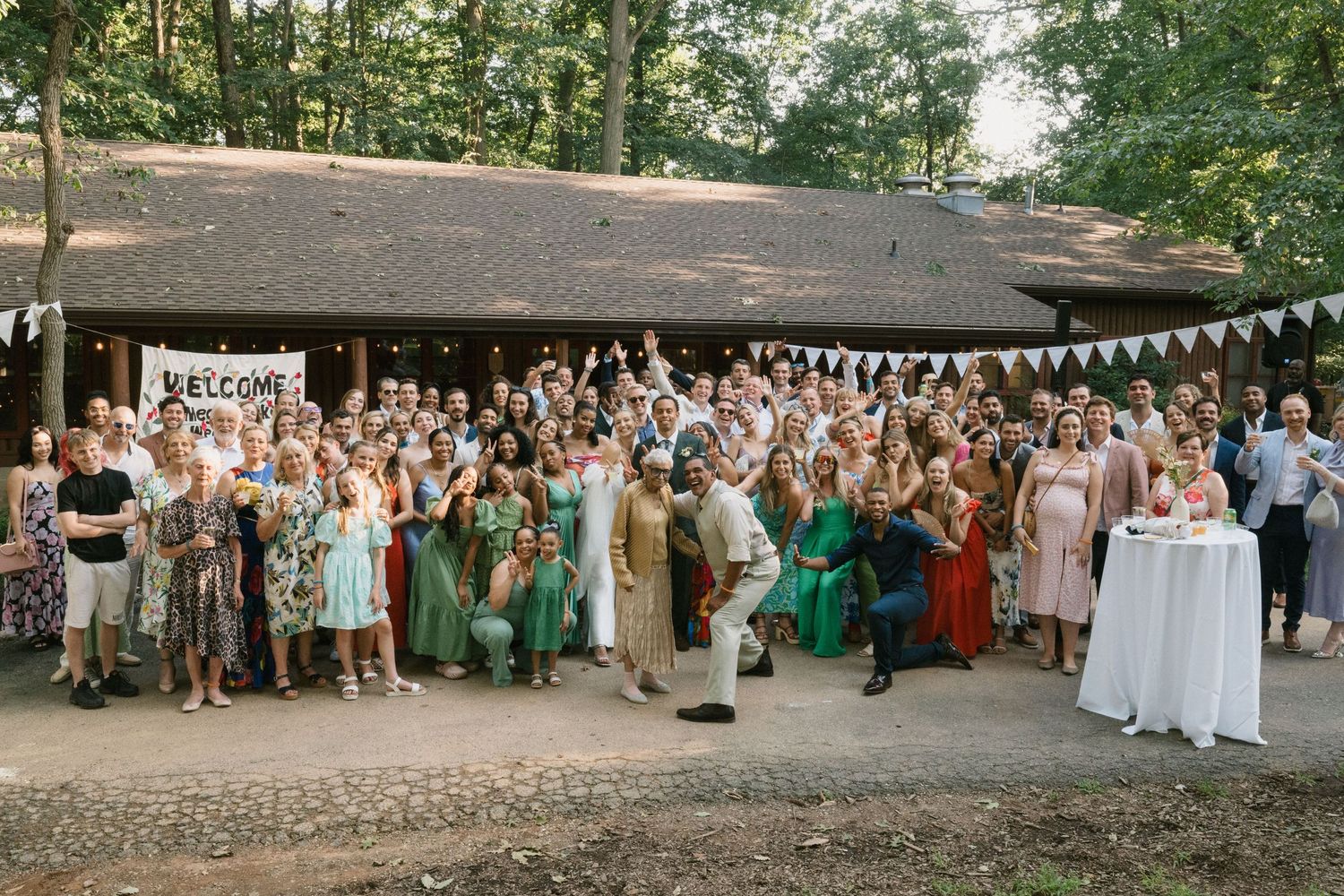 Large group photo of wedding guests gathered under a rustic pavilion with bunting decorations.