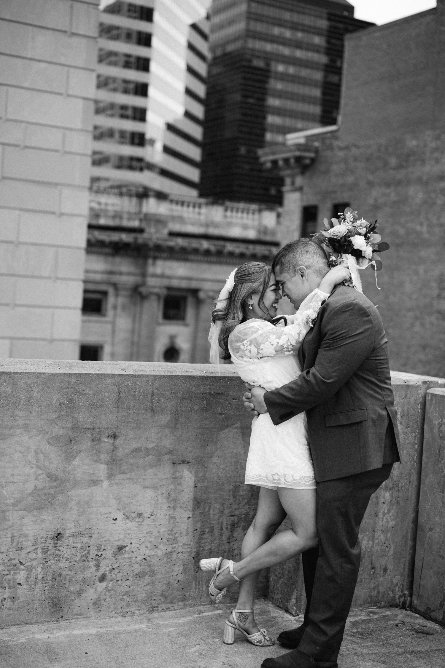 A romantic black and white wedding photo of a couple sharing an intimate moment against an urban backdrop.