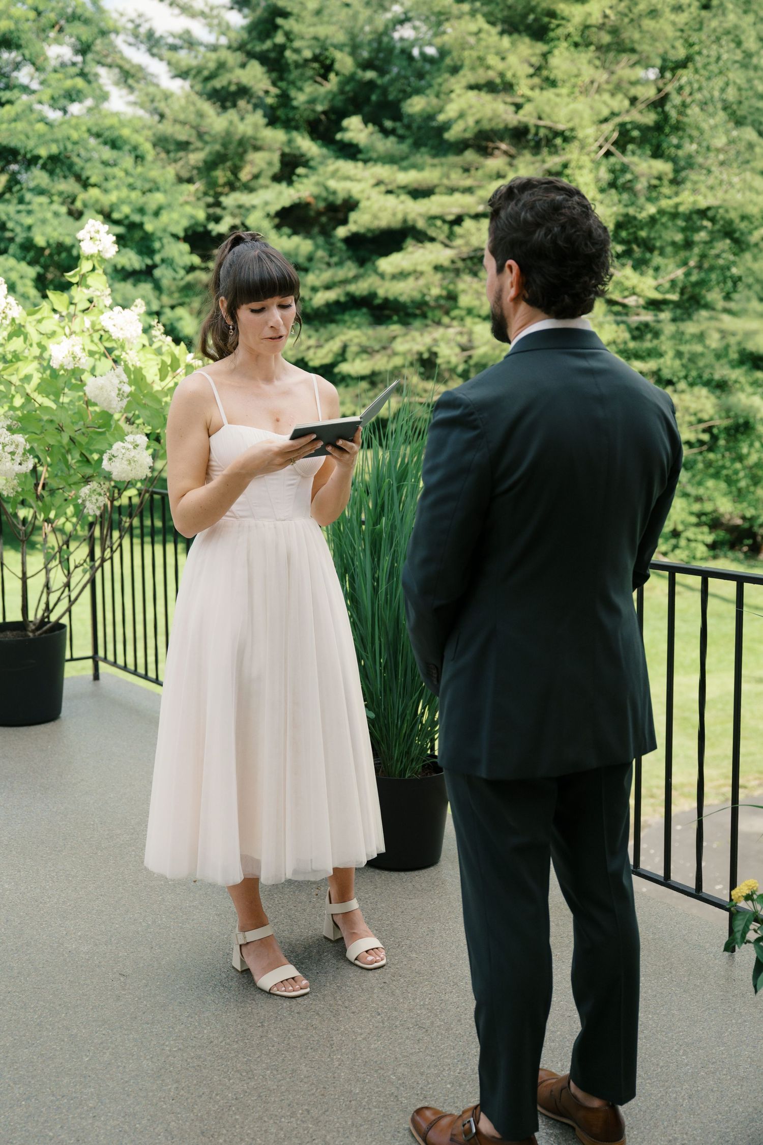 Couple exchanges wedding vows on an outdoor patio surrounded by lush greenery and potted plants.