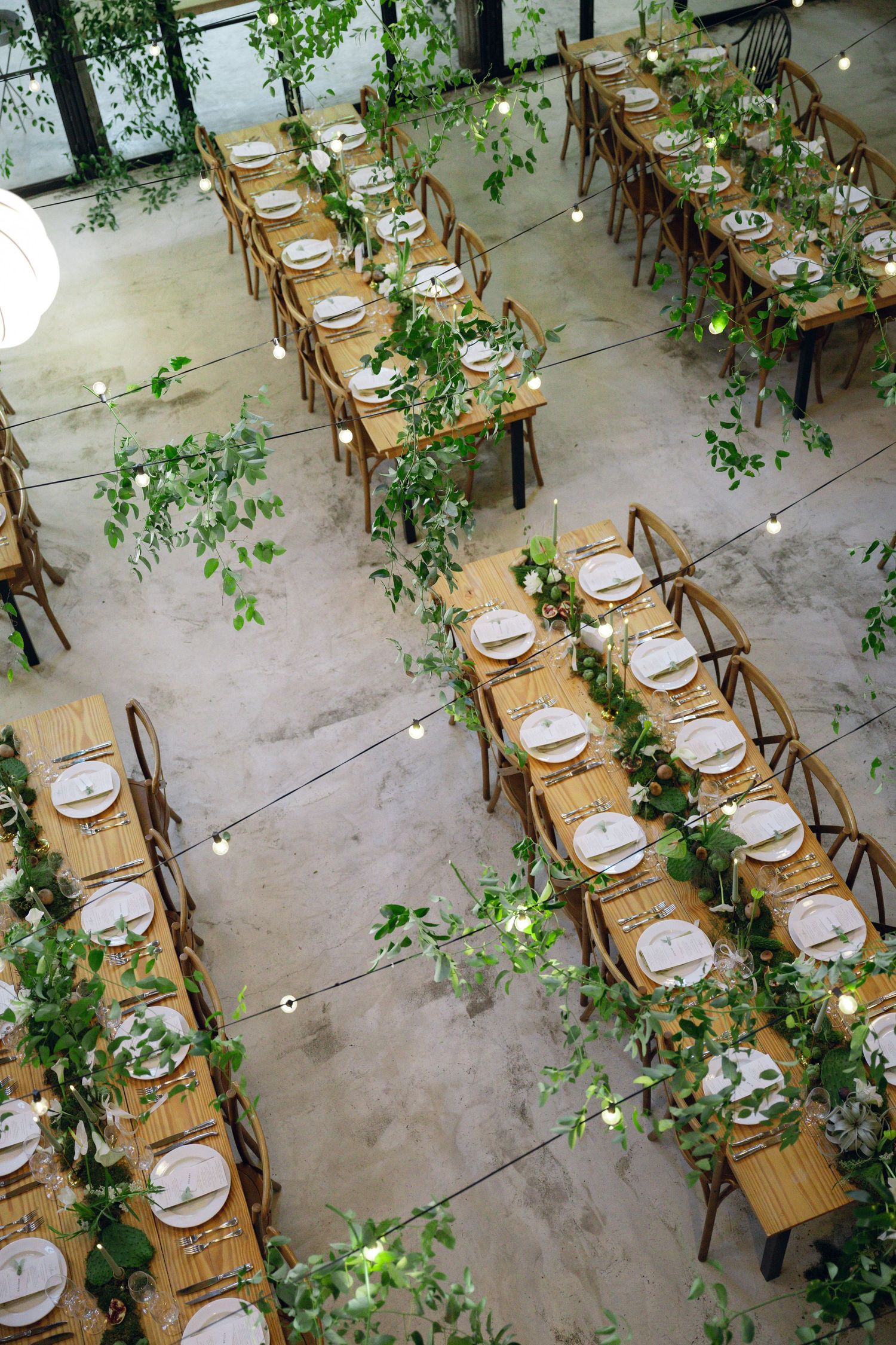 Rustic wooden tables decorated with greenery and place settings for an elegant outdoor wedding reception.