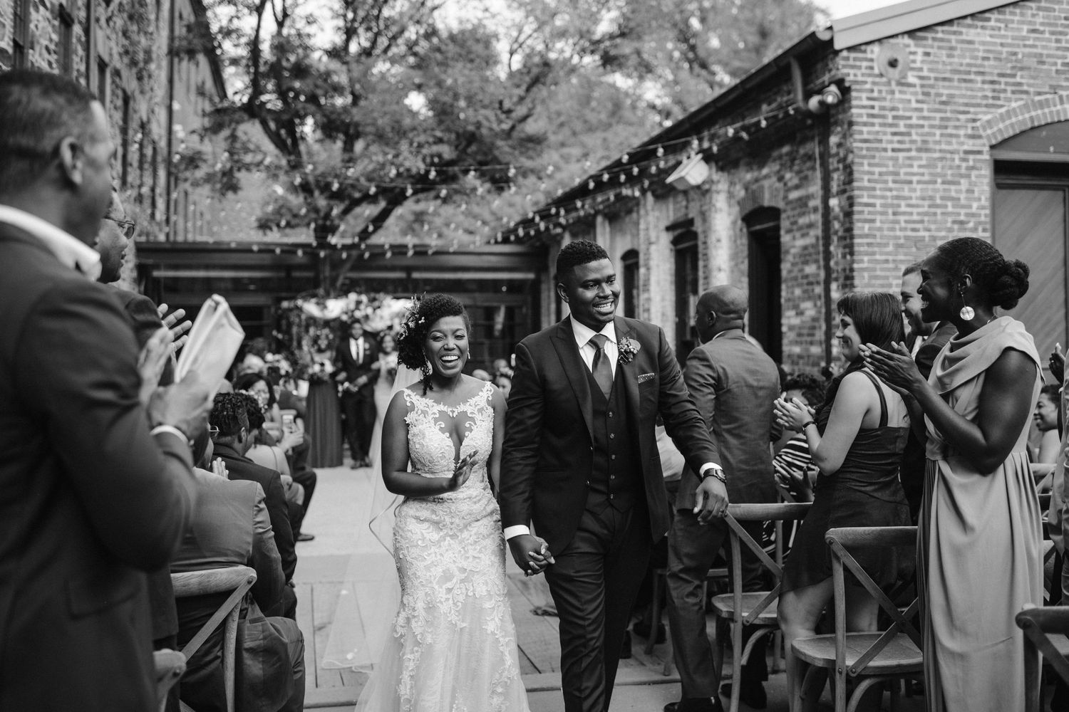Wedding guests mingle and socialize during an outdoor reception by a brick building.