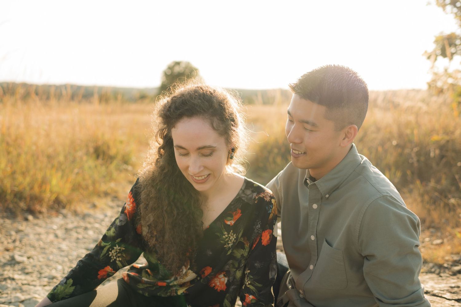 Couple embracing in golden field during sunset photoshoot with warm lighting.