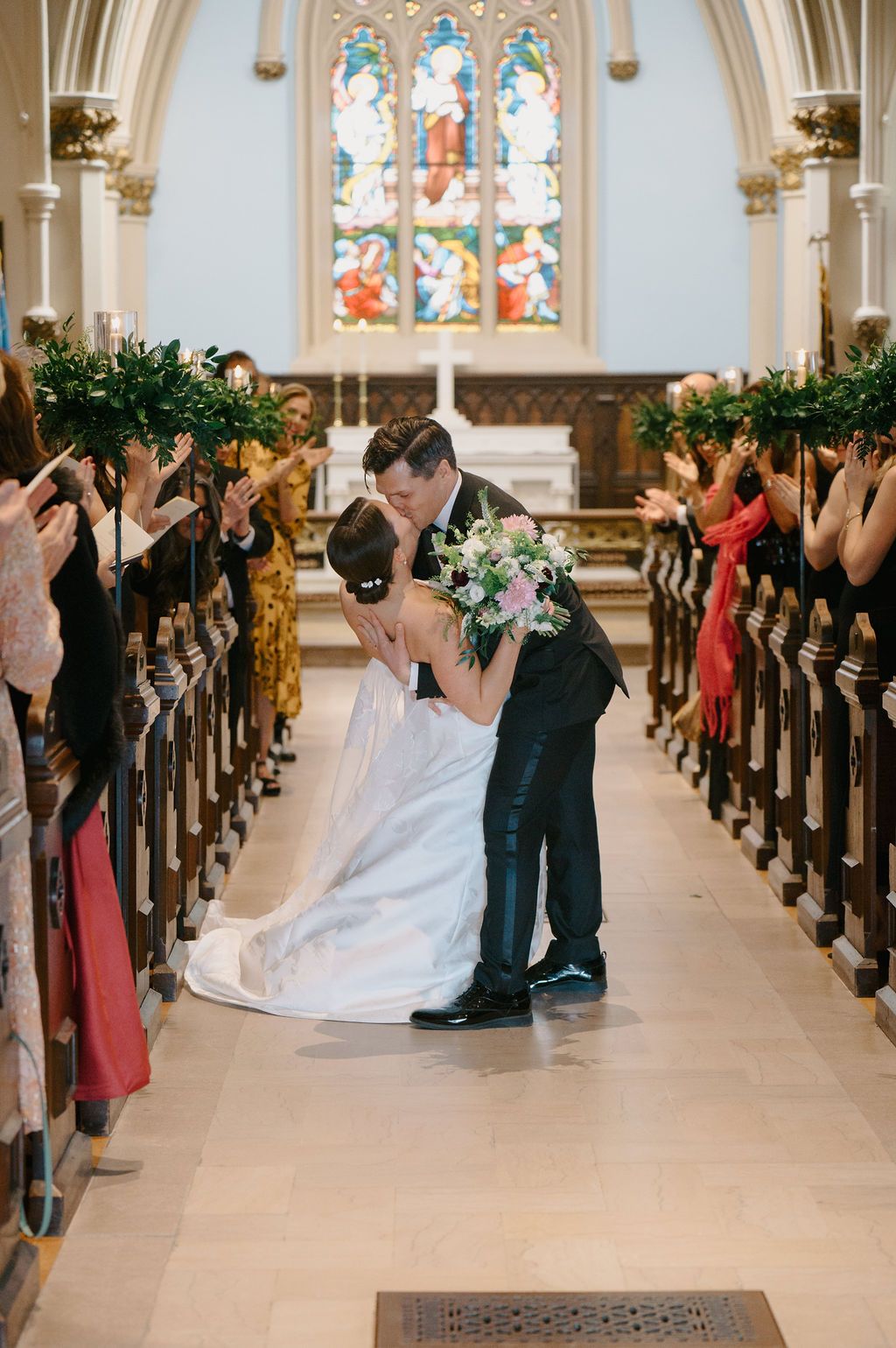 Wedding celebration in a bright church with guests lining the pews as the couple shares their first kiss.