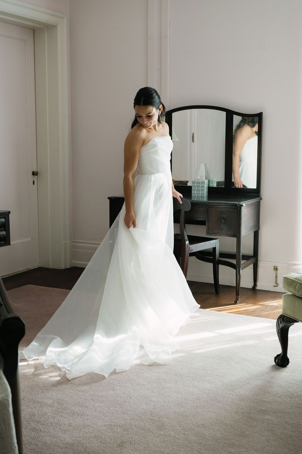 A flowing white wedding gown photographed in a bright room with mirrors and natural light.