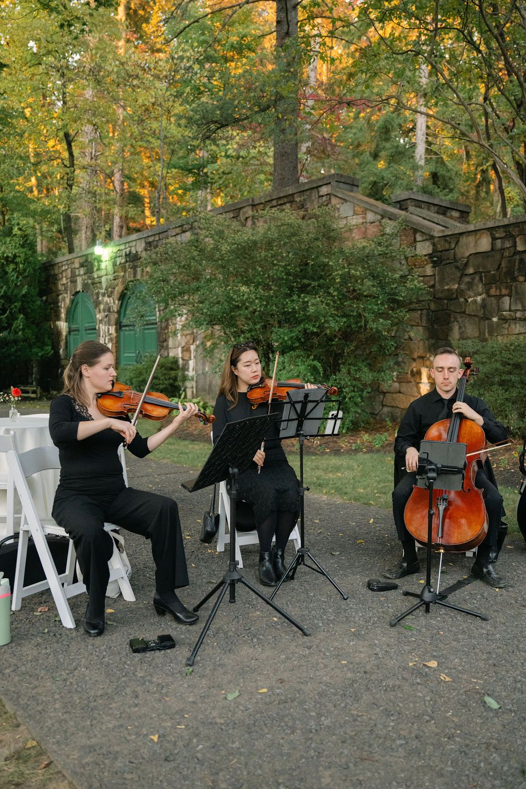 String quartet performing outdoors in formal attire among autumn trees.