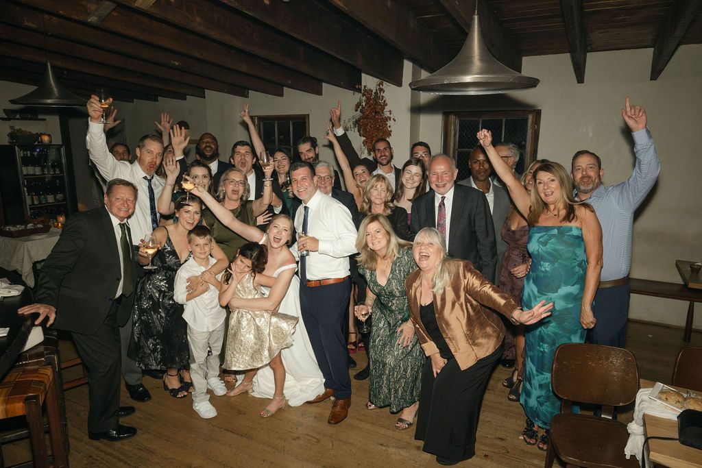 Large group of wedding guests posing together for a celebratory photo in a rustic venue.