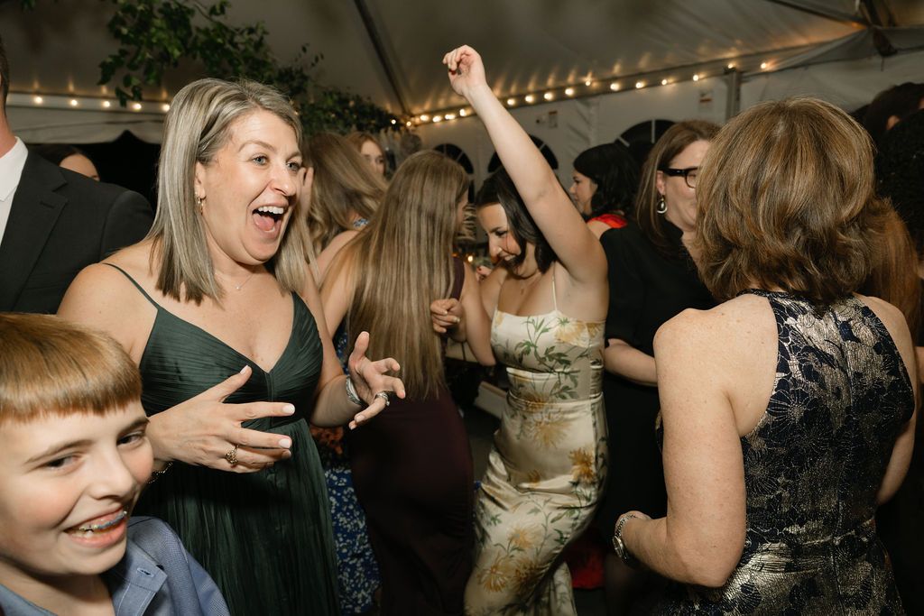 Energetic wedding guests dancing and celebrating at a reception under string lights.