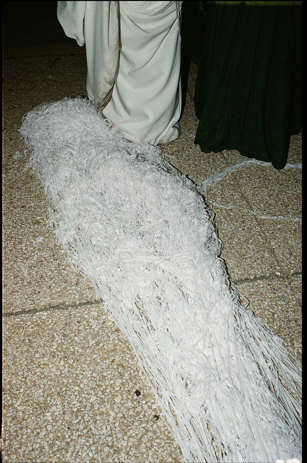 A shredded pile of white paper documents scattered across a floor next to someone wearing light colored clothing.