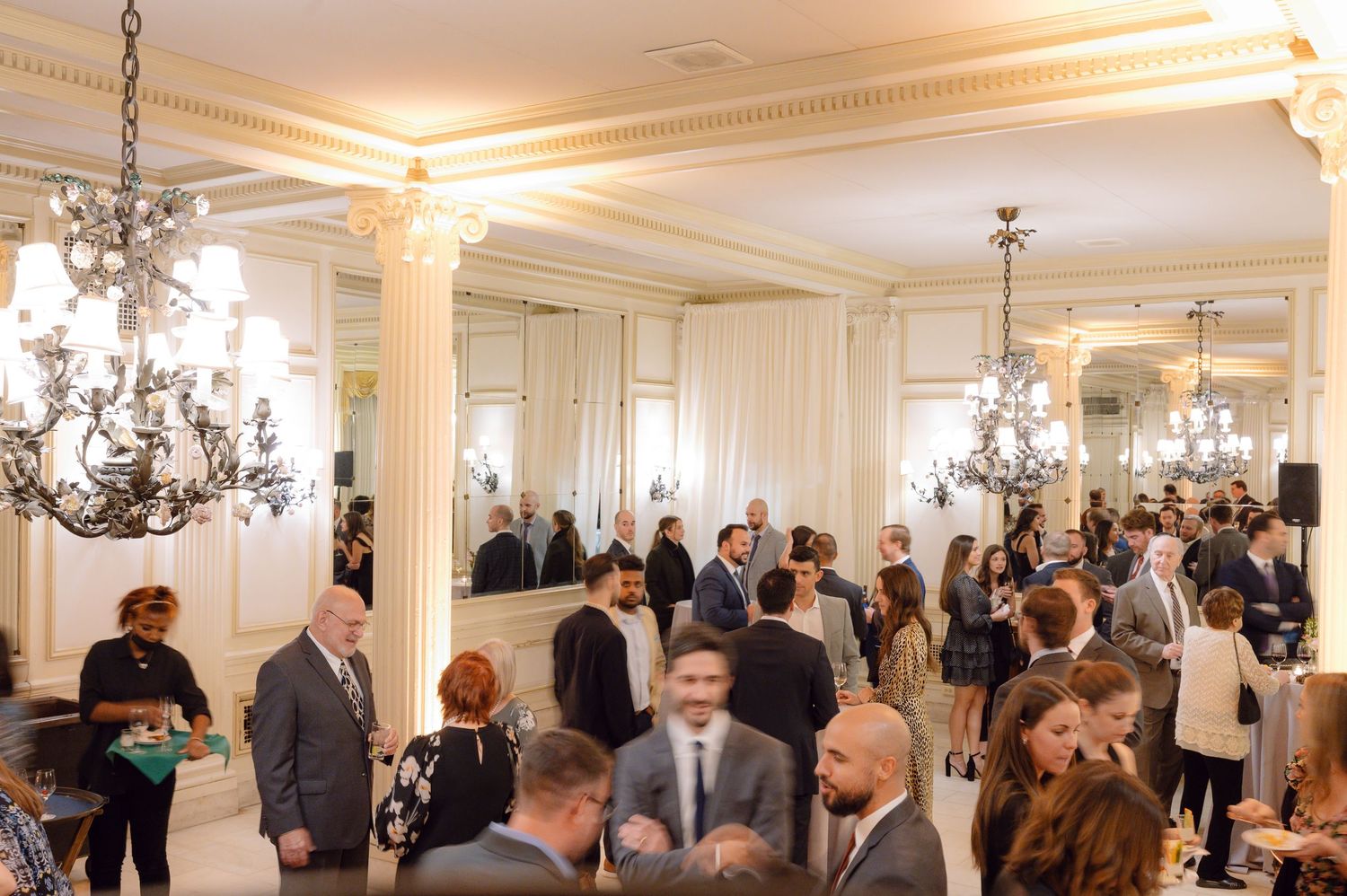 Elegant wedding reception venue with white columns and chandeliers filled with guests.