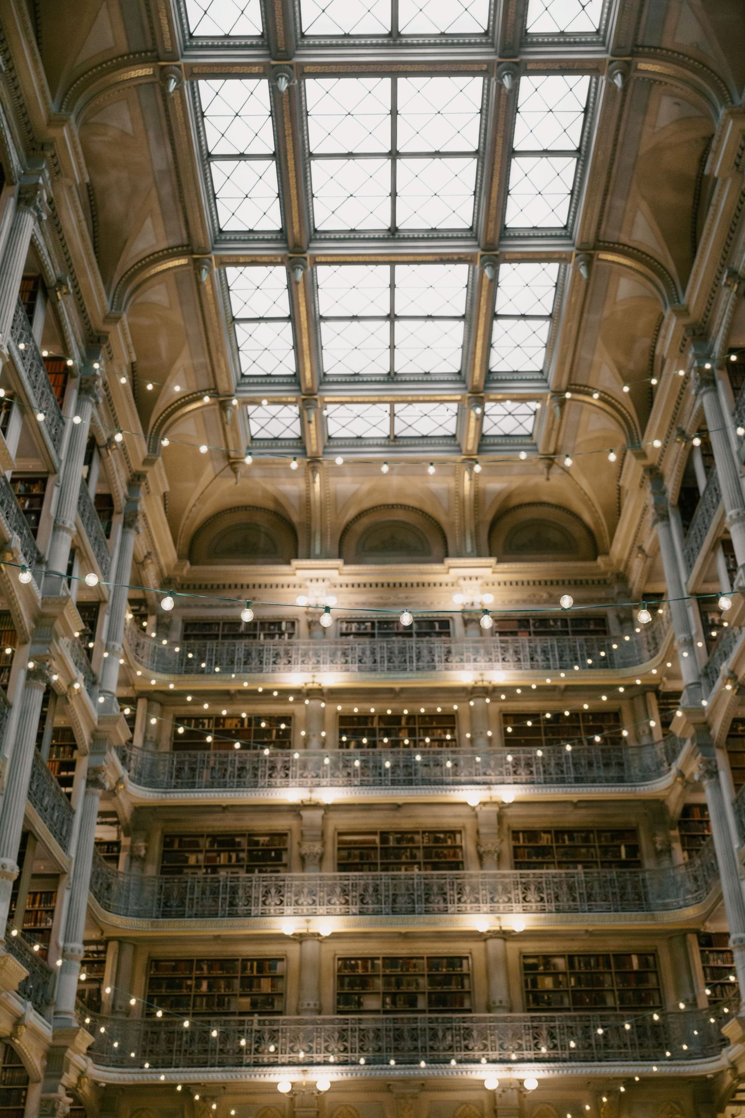 Historic library interior with multiple levels, string lights and ornate architectural details.