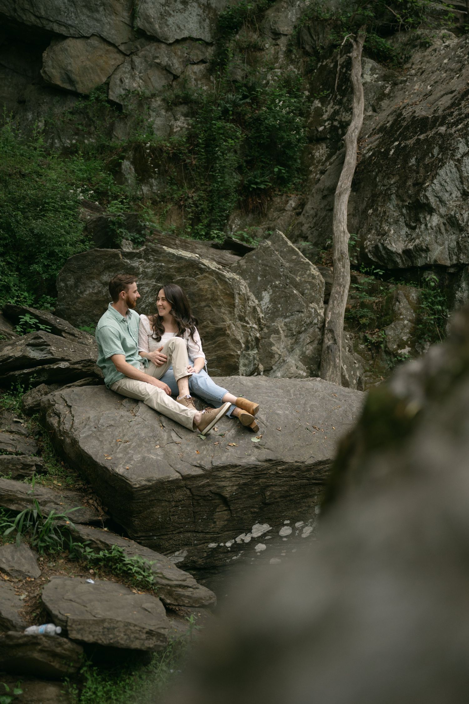A couple shares an intimate moment on large rocks near a scenic waterfall.