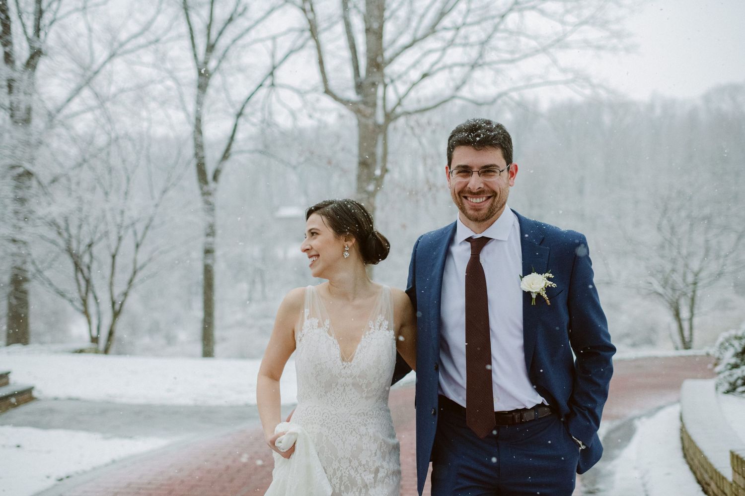 A couple shares a joyful moment on a snow-covered walkway during their winter wedding.