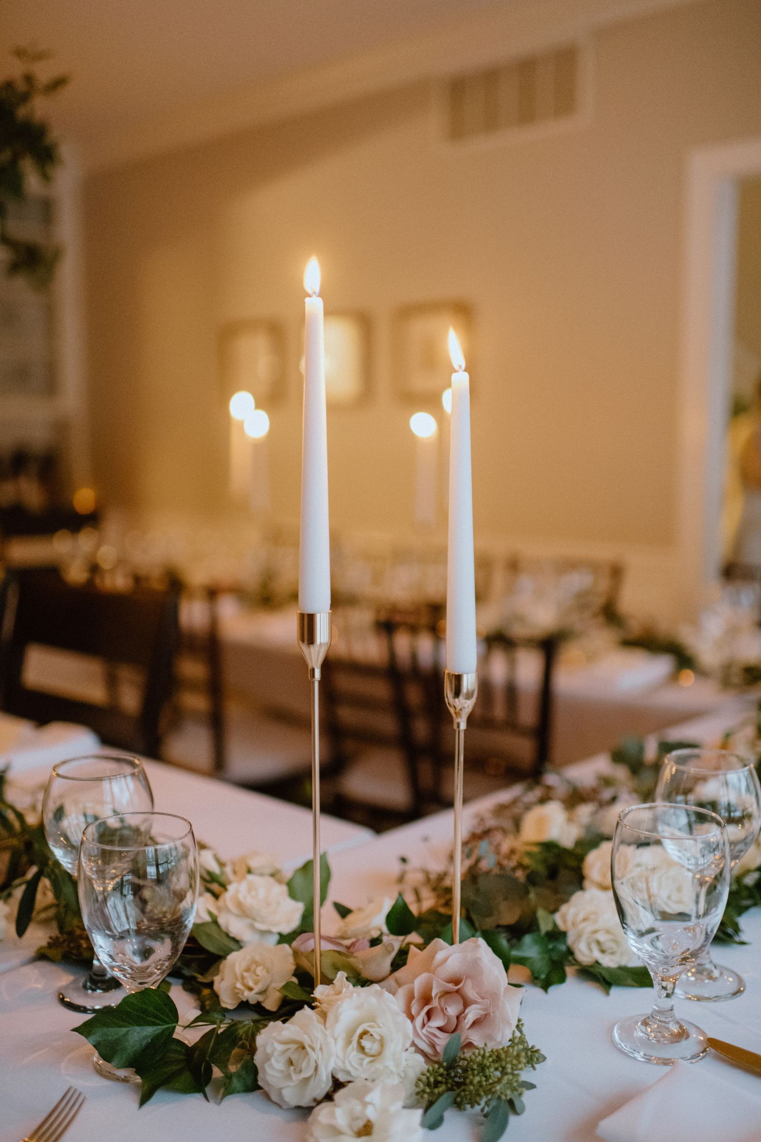 Elegant table centerpiece featuring white candles and blush roses on crisp linens.