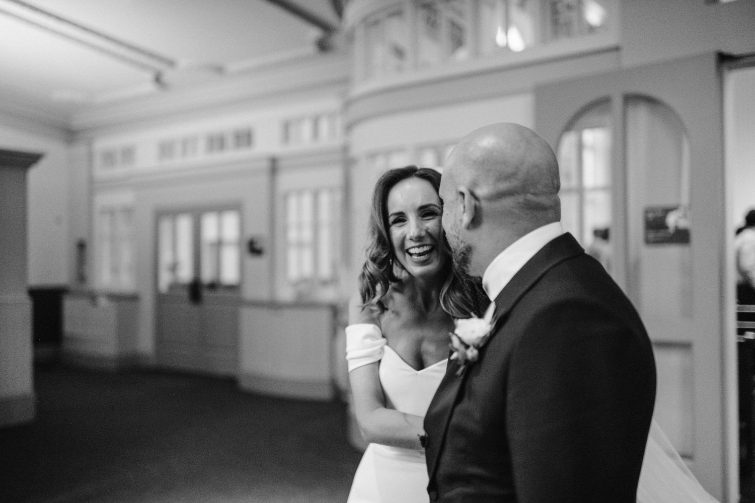 A candid black and white moment of an emotional couple sharing laughter in an elegant venue.