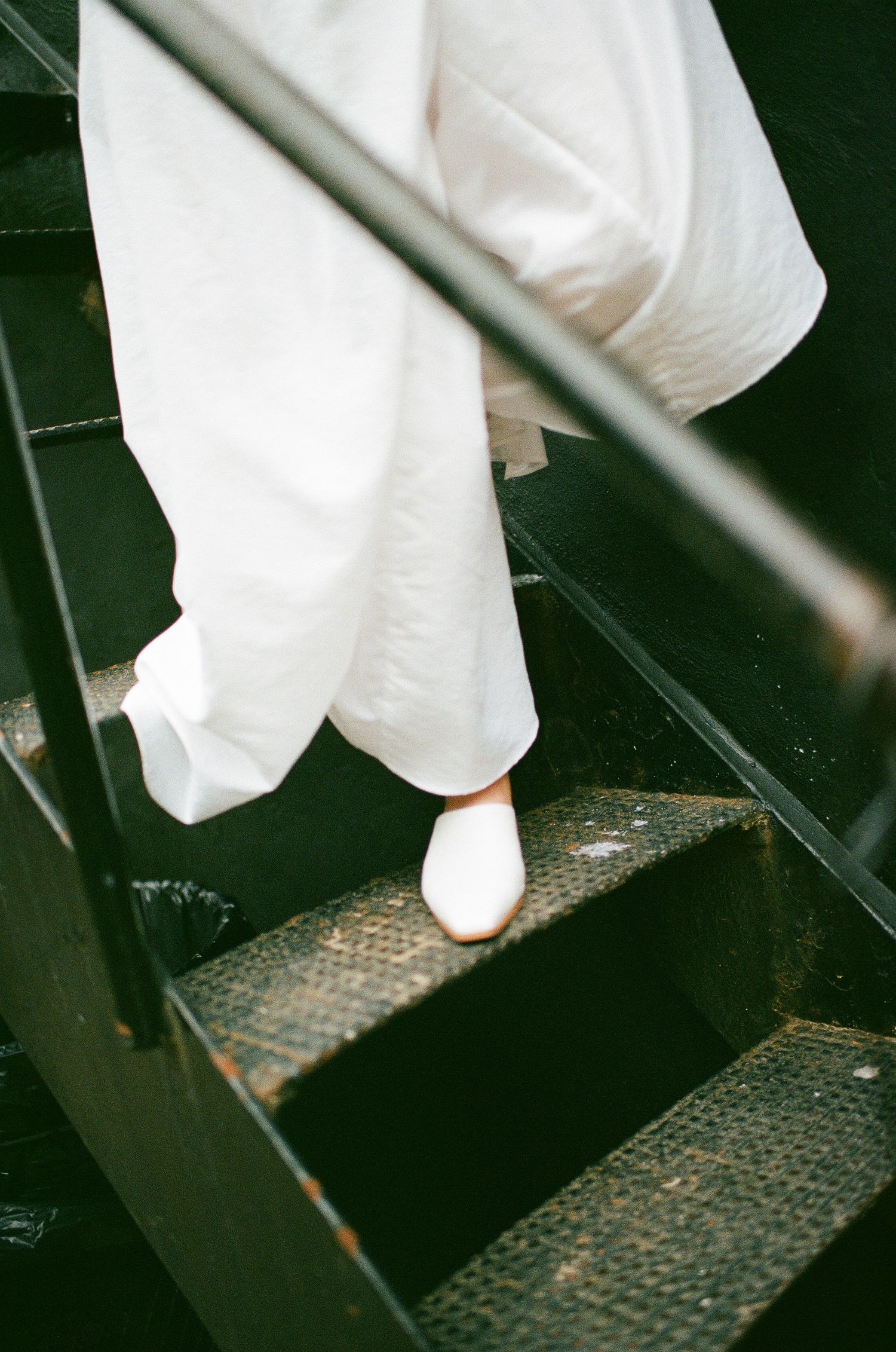 A person in flowing white clothing and white shoes descending dark metal stairs.