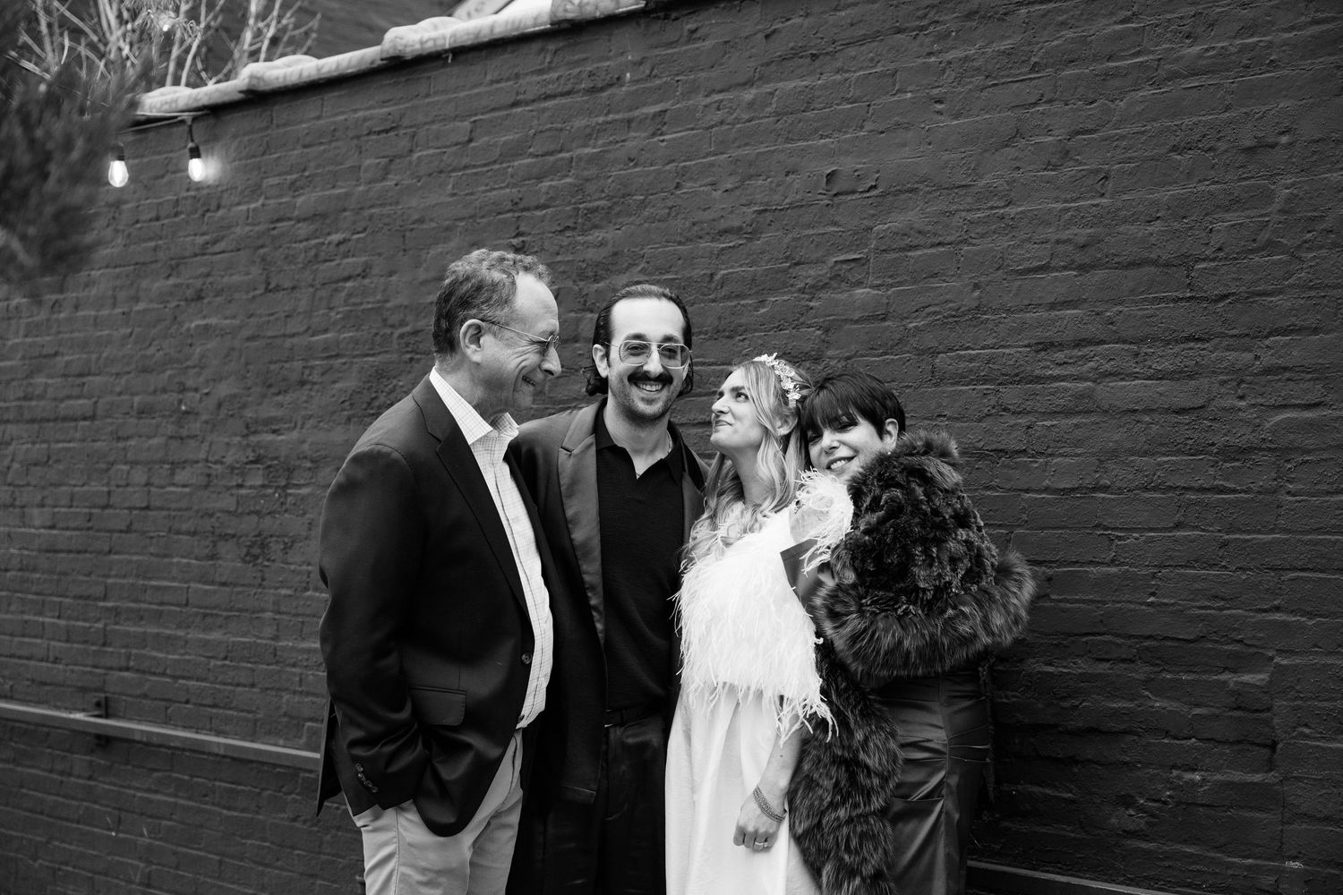 Black and white wedding photo of a small group sharing a candid moment against a brick wall at Fadensonnen in Baltimore