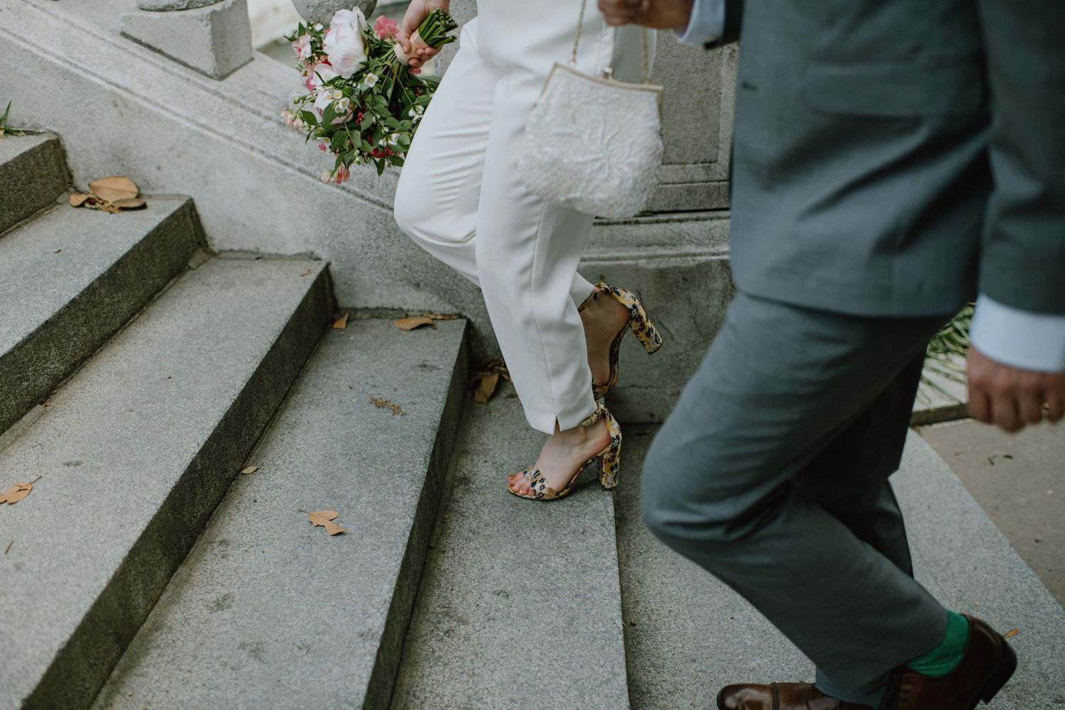Wedding couple's feet walking up stone steps, bride in white dress and heels.