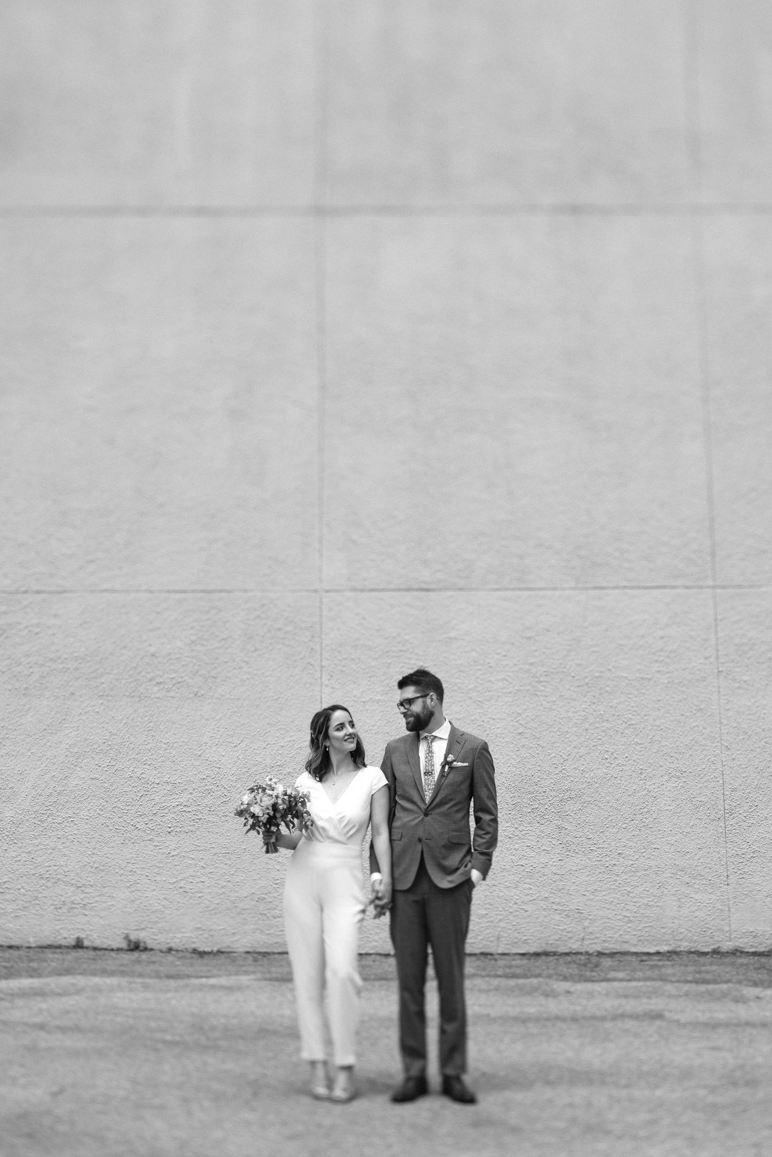 Couple walking down urban sidewalk in wedding attire.