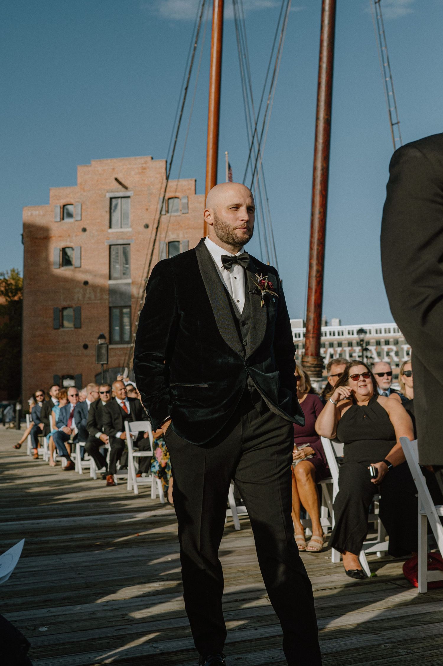 Wedding ceremony setup on wooden pier with historic brick building in background.