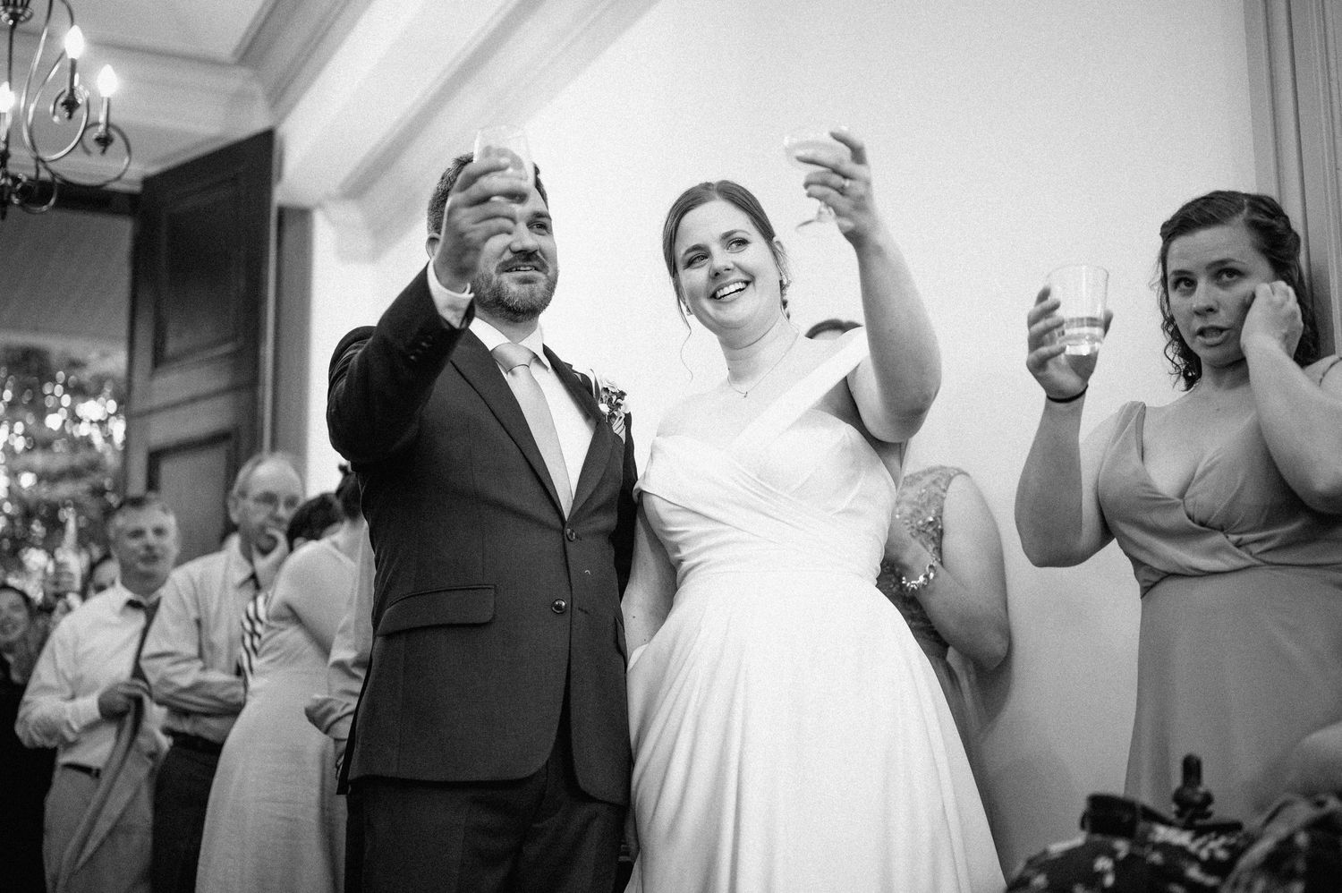 Black and white candid photo of wedding celebration with people dancing and raising glasses.