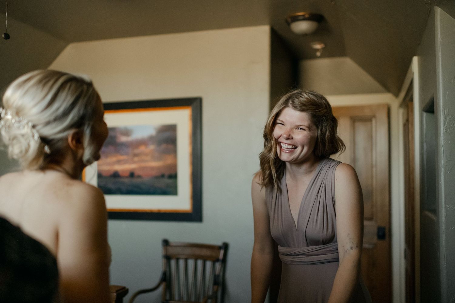 Two people share a joyful moment in a room with a sunset painting on the wall.