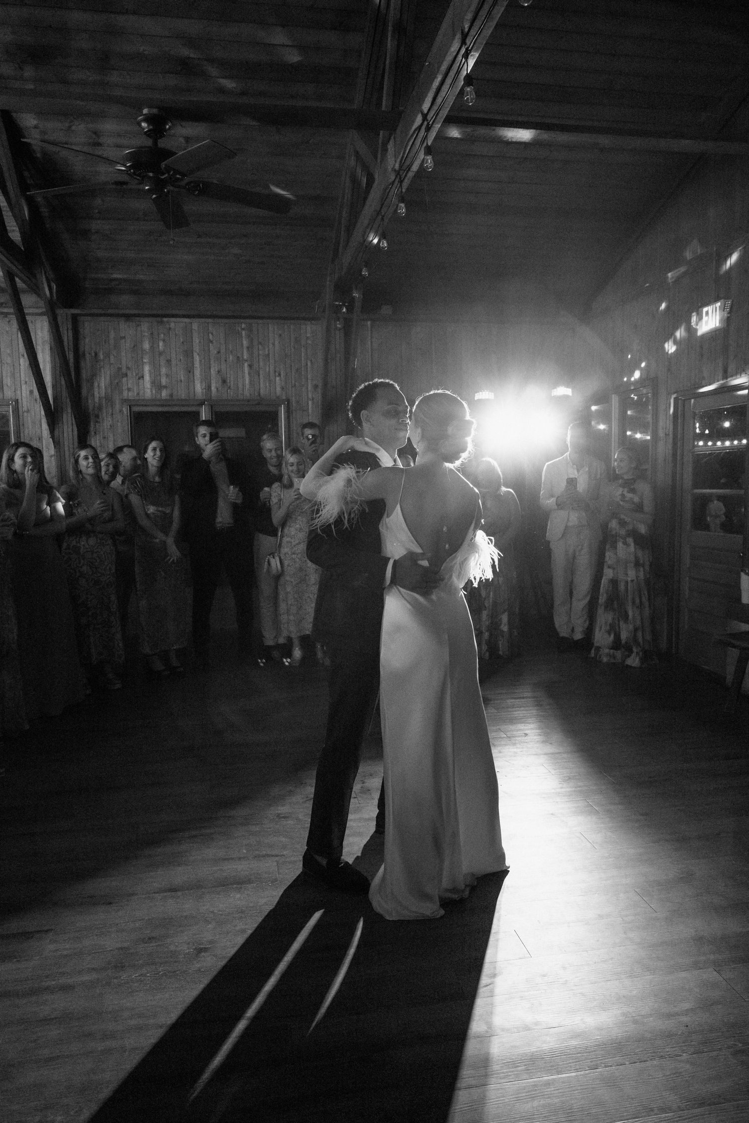 A couple shares their first dance at a rustic wedding reception with dramatic backlighting.