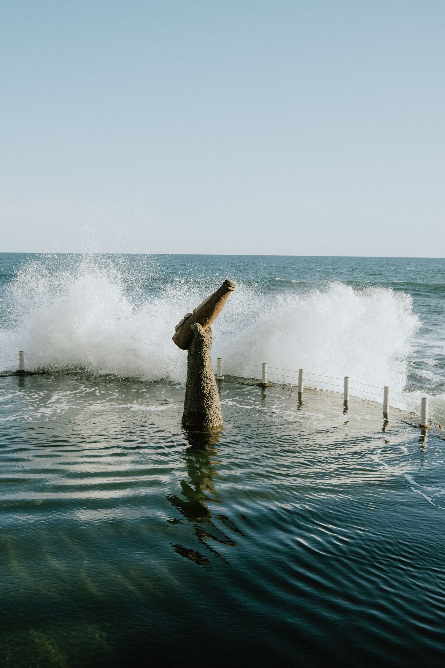 Waves crash against a concrete post in the ocean creating dramatic splashes.