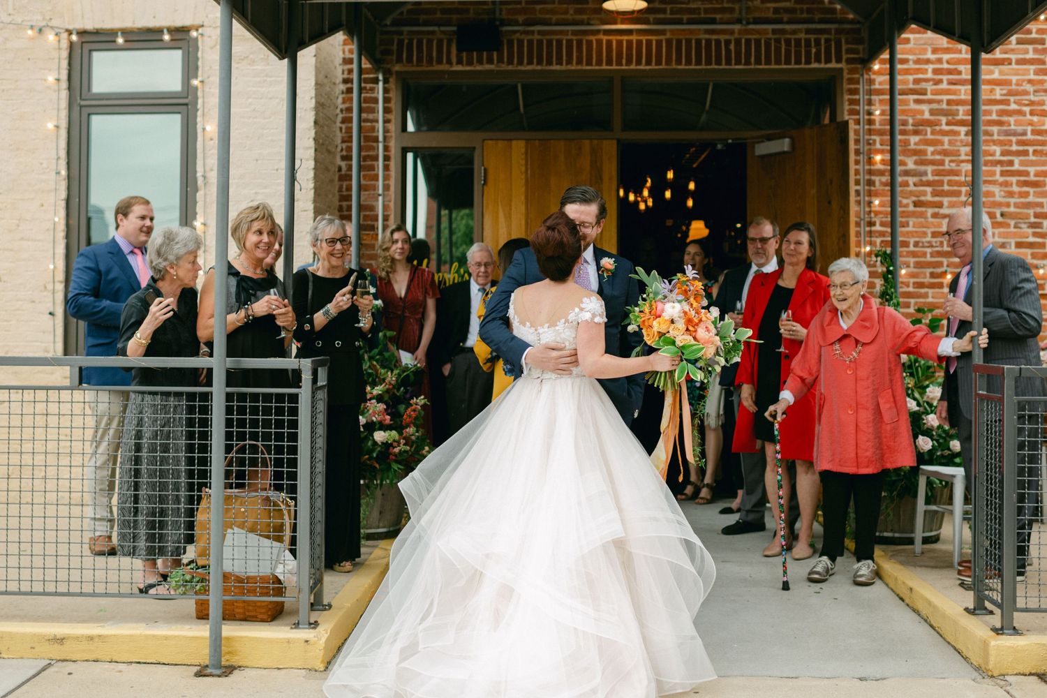 Wedding celebration with guests watching from railings as couple exits brick building.