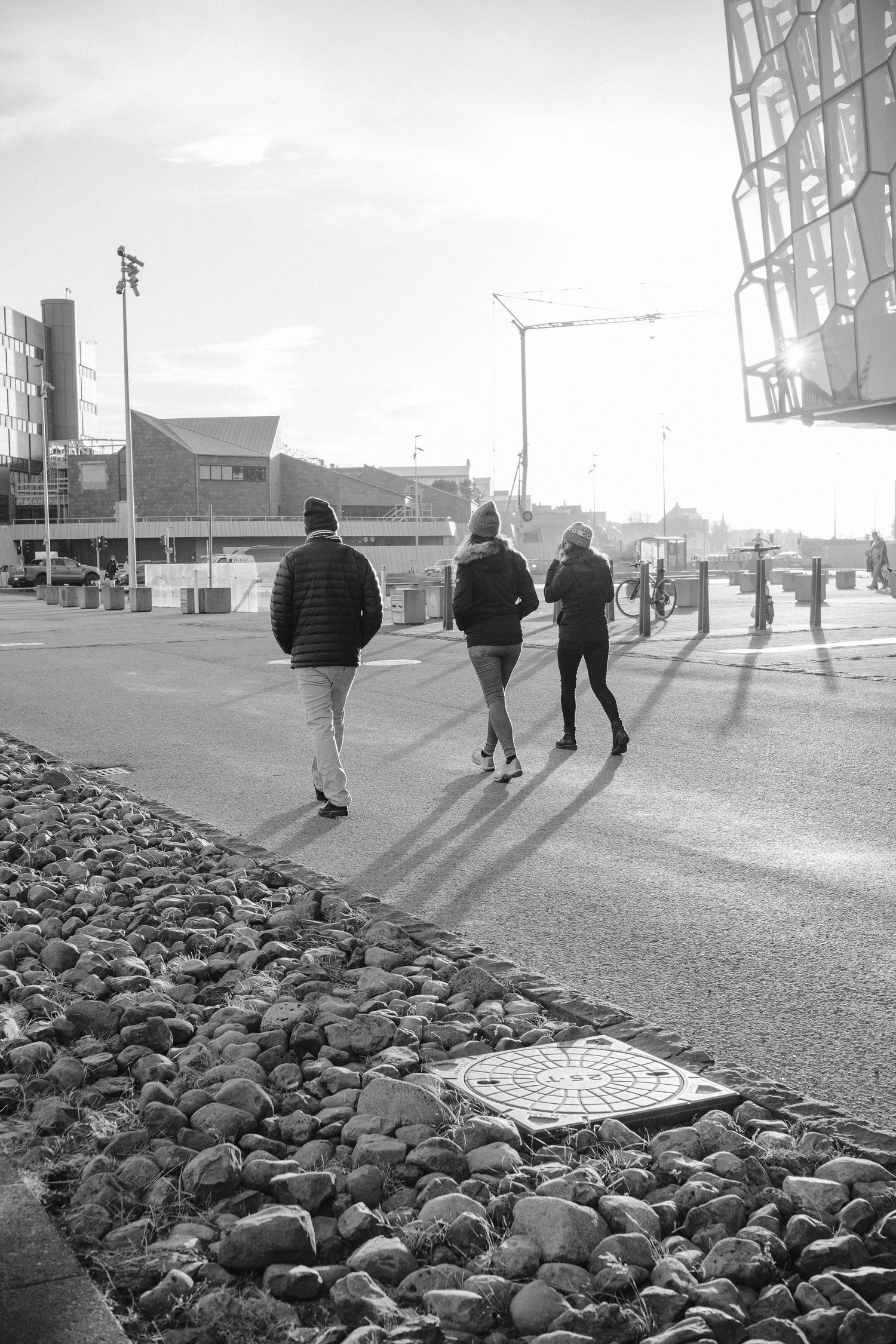 People walking along urban waterfront with rocks and buildings in black and white.