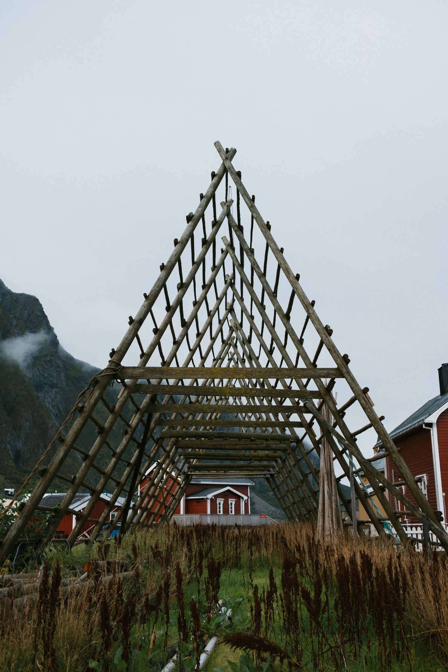 Traditional wooden fish drying rack structure frames a red cabin in a Norwegian fjord landscape.
