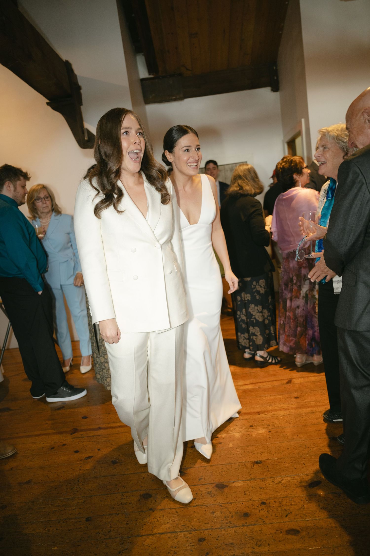 Wedding guests mingling and dancing on a hardwood floor at an indoor reception venue.