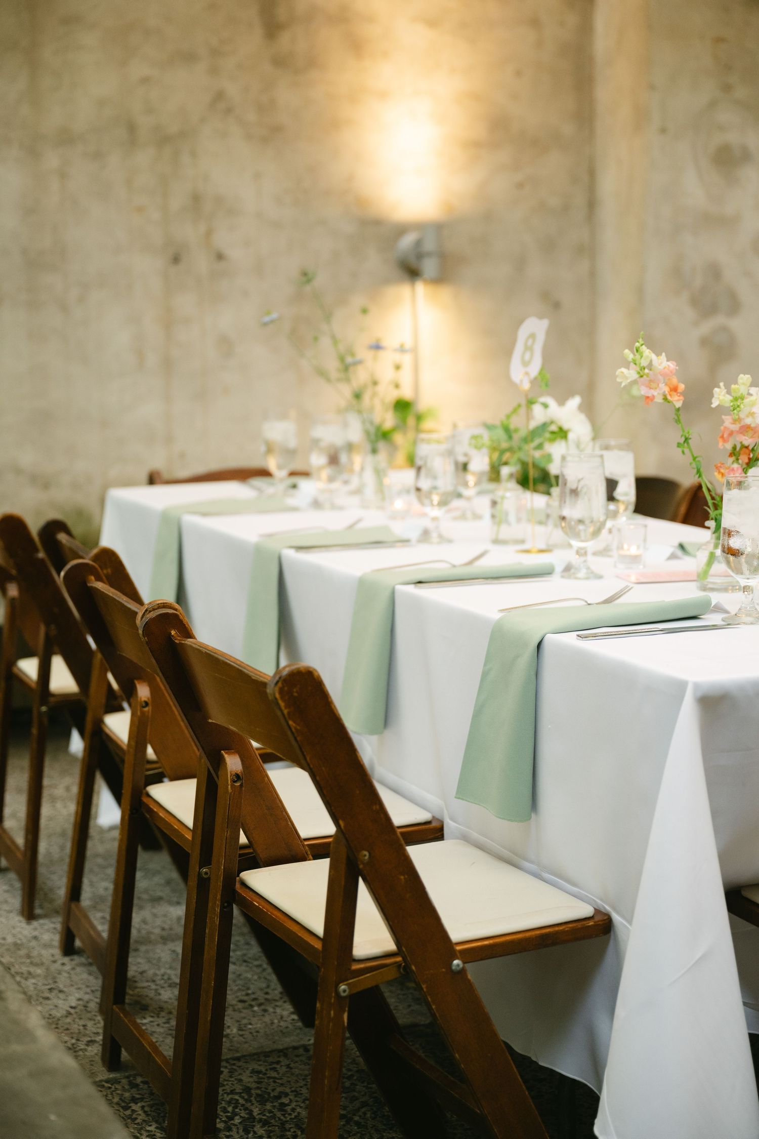 White linen tablecloths and rustic wooden chairs create an elegant table setting for a wedding reception.