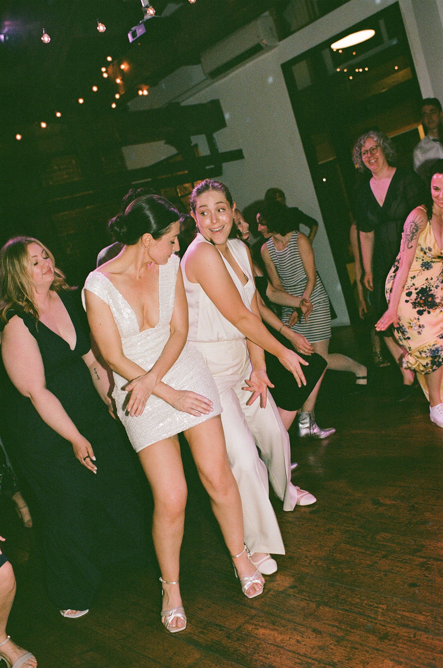 People in white clothing dance together on a wooden floor at a lively party event.