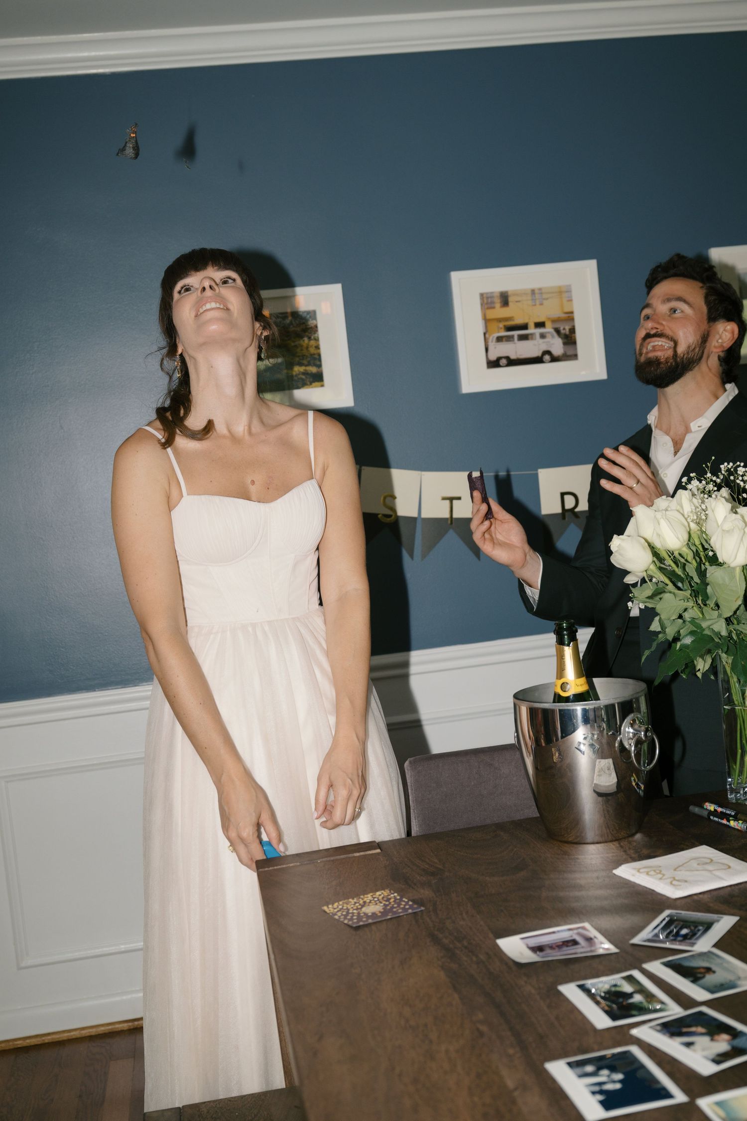 A joyful candid moment at a party with people in formal attire laughing near a table with photographs and champagne.