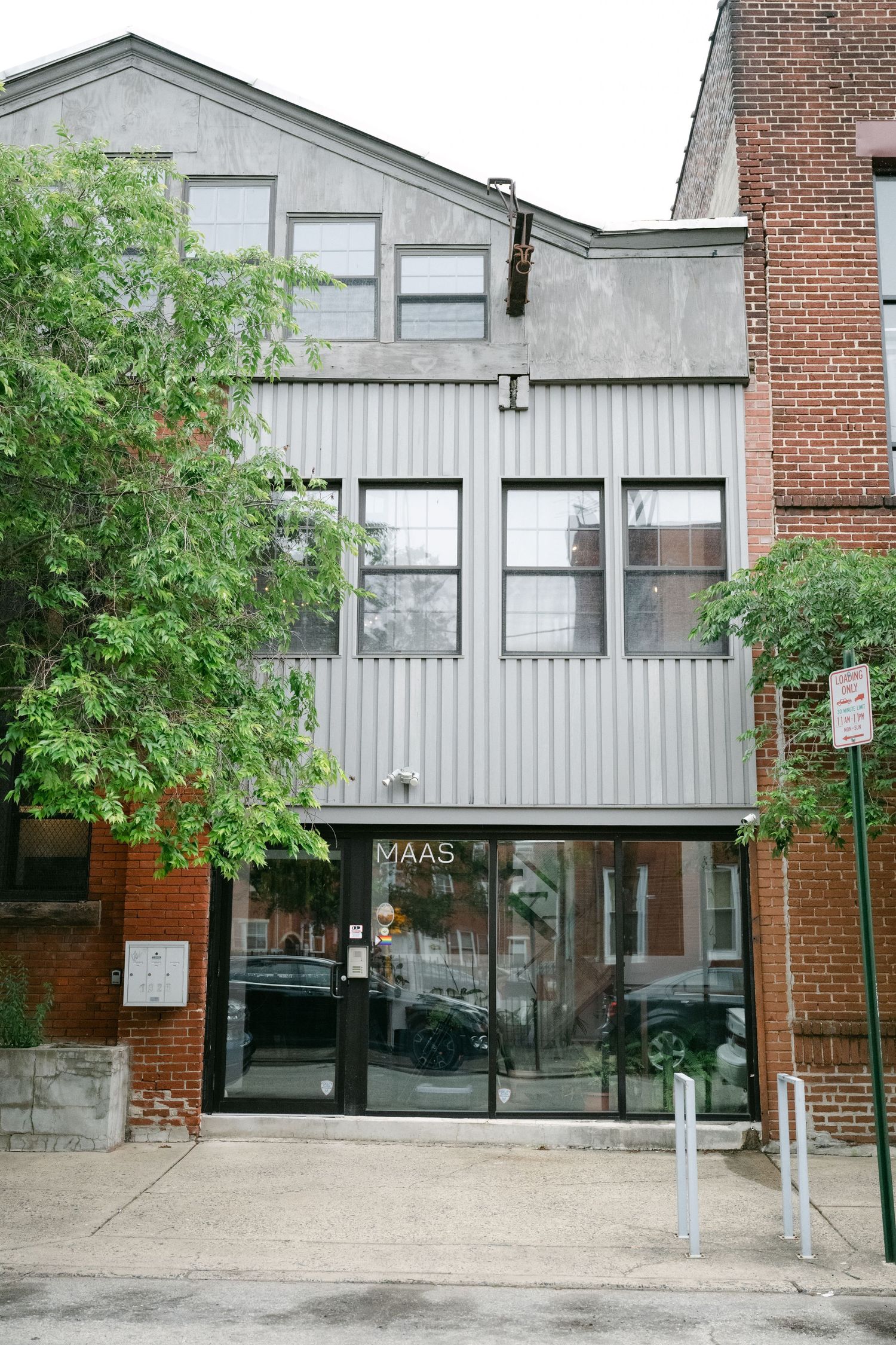 Modern three-story building exterior with gray vertical siding, brick elements, and glass entrance doors on a city street.