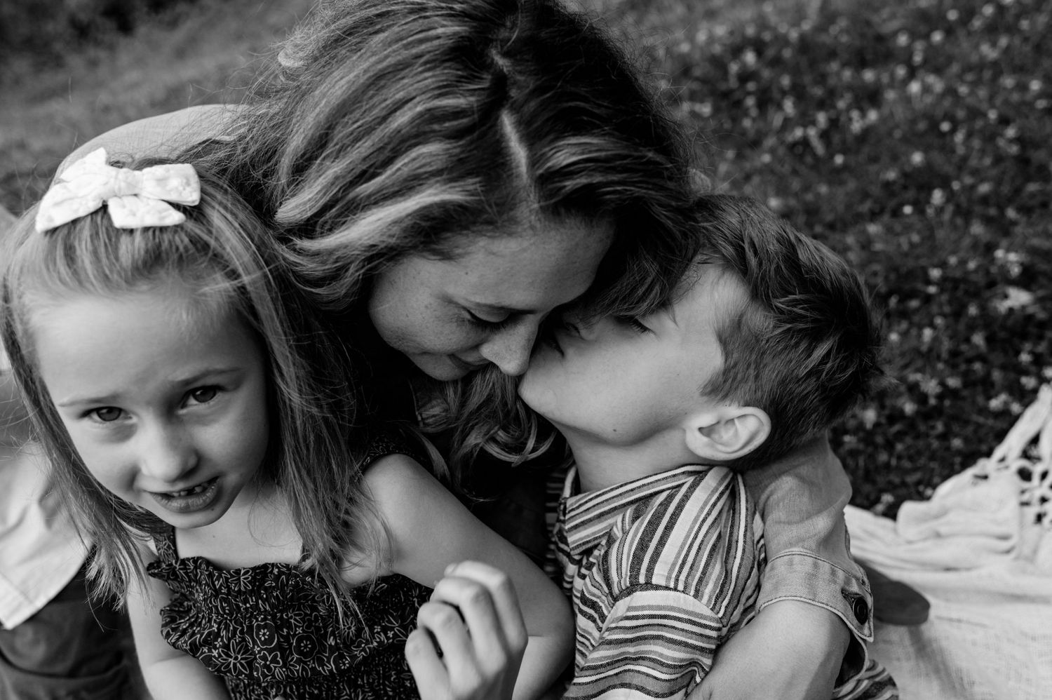 Black and white portrait showing affectionate family embrace and smiles during outdoor photo session.
