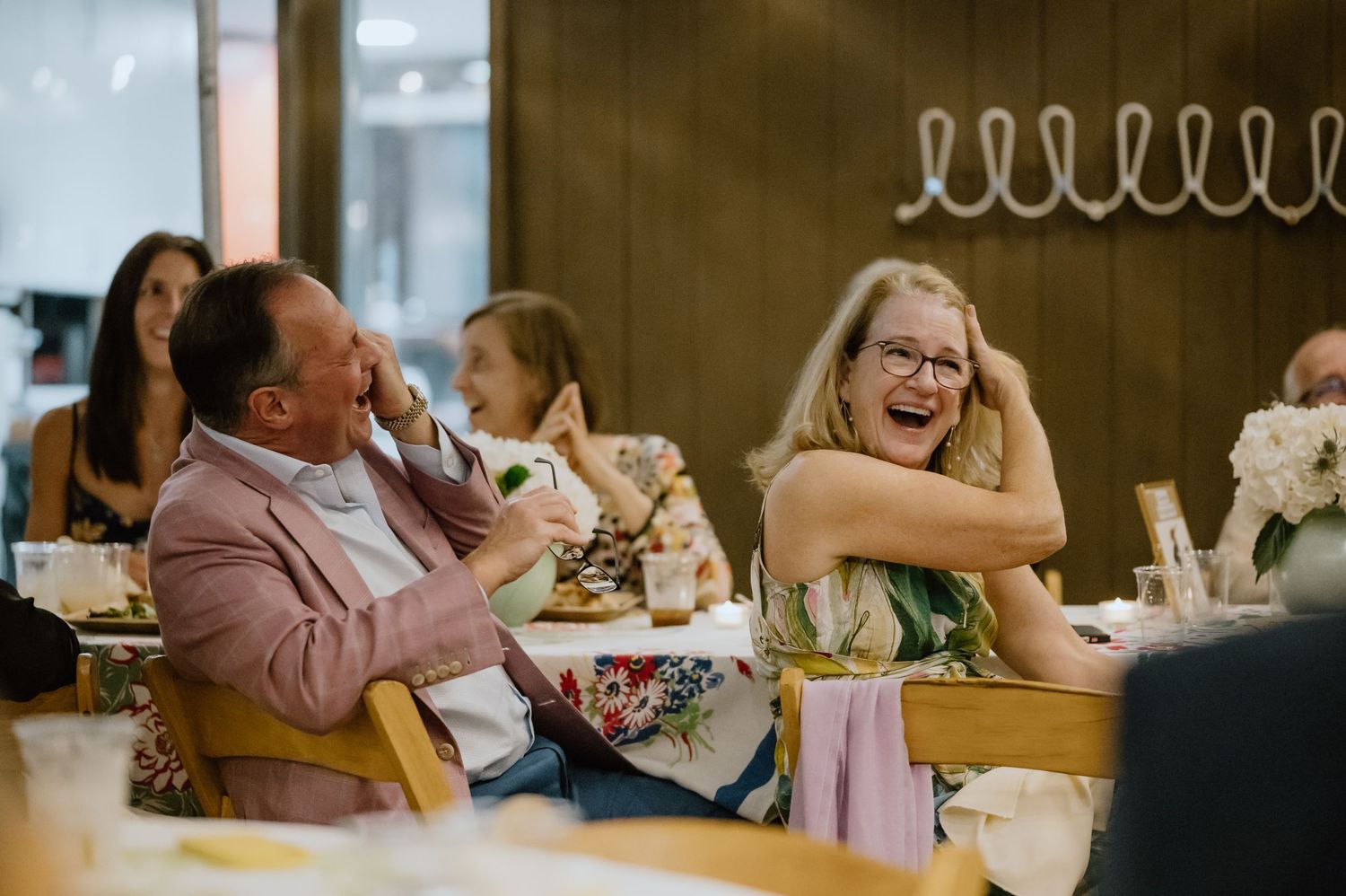 Candid moment of guests laughing heartily during a celebratory dinner event.
