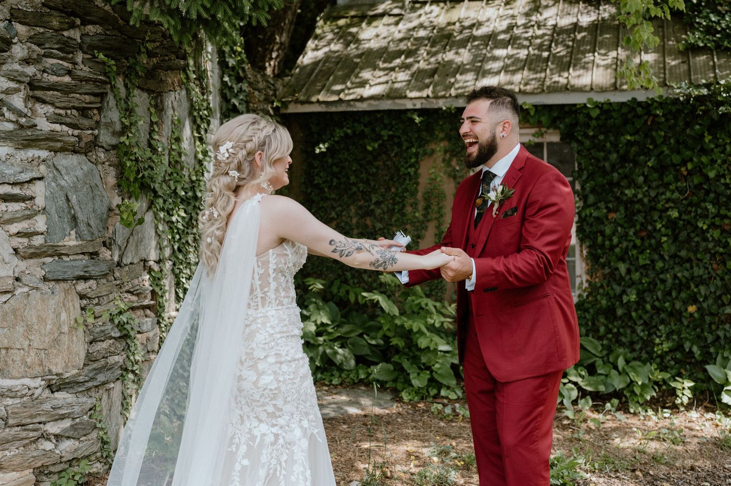 A couple shares a joyful moment in front of an ivy-covered stone wall during their wedding.