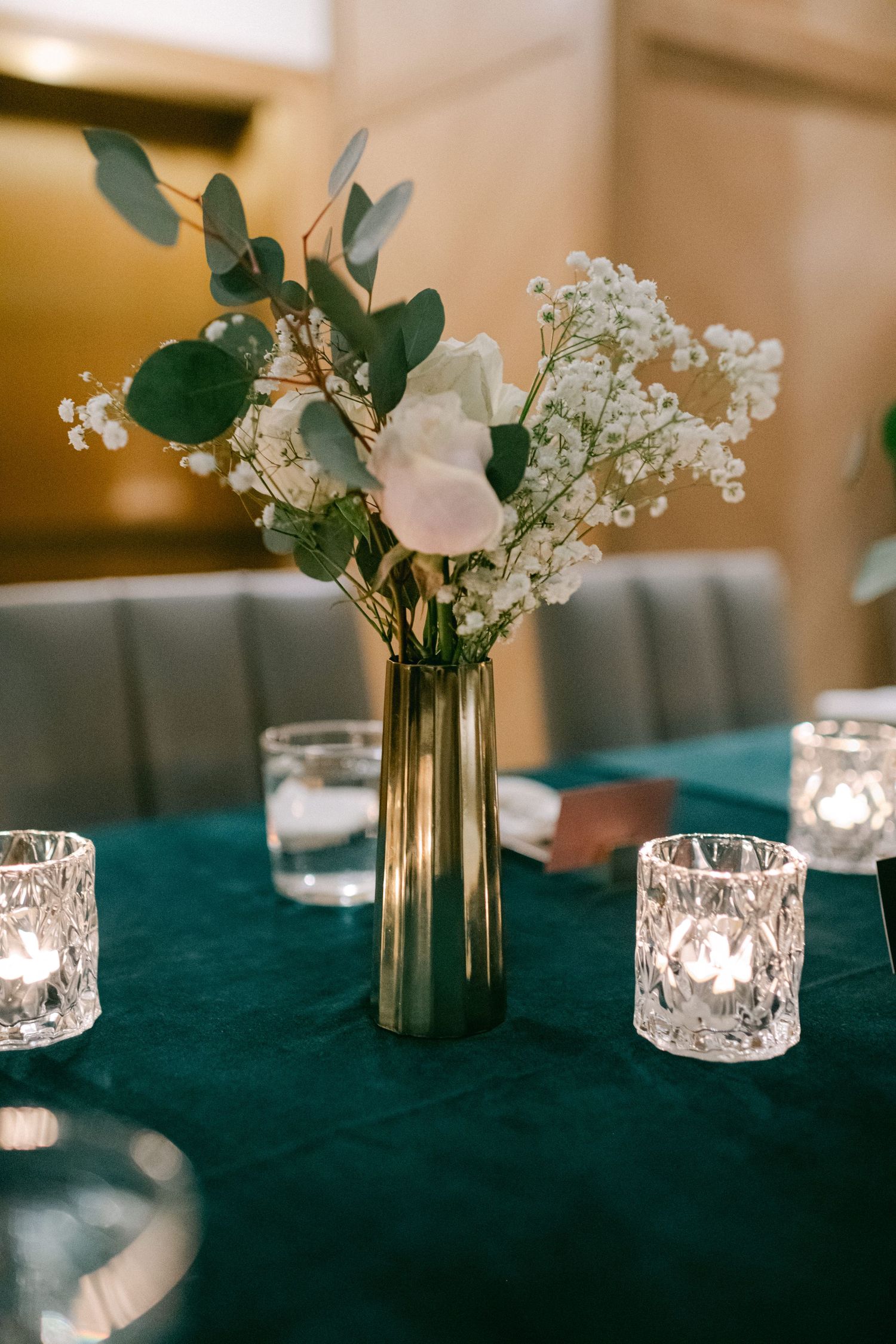 Elegant centerpiece with eucalyptus, baby's breath and white flowers in gold vase with crystal votives.