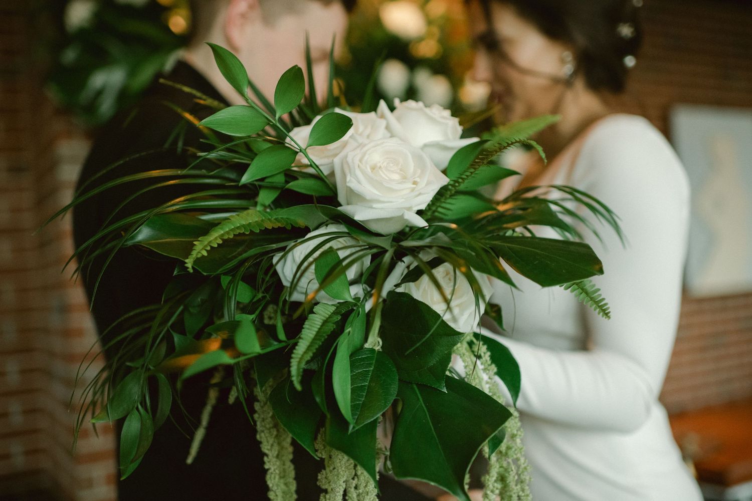 Close-up of tropical greenery and white rose wedding bouquet arrangement.