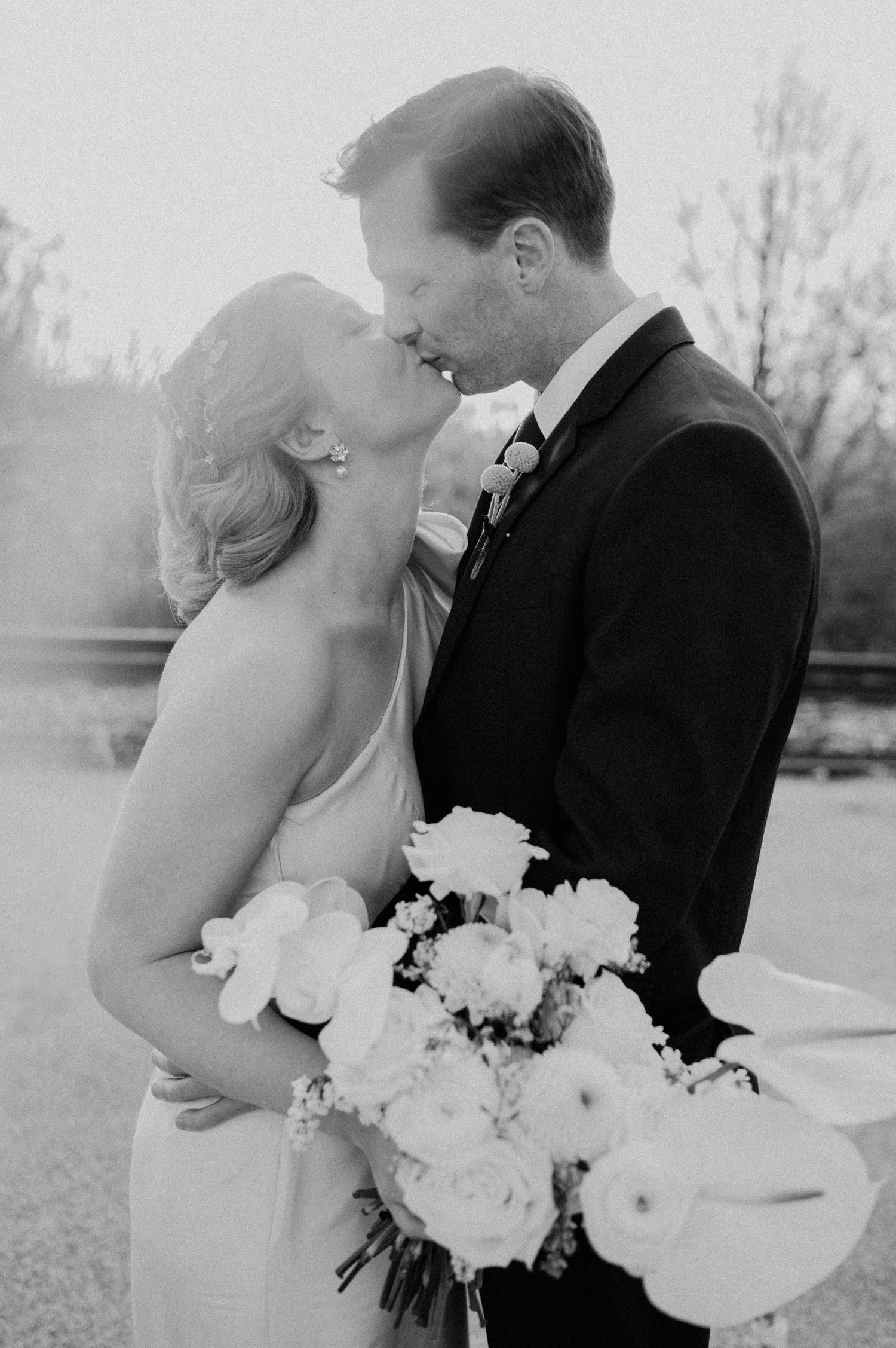 Black and white intimate portrait of newlyweds sharing romantic moment with bouquet.