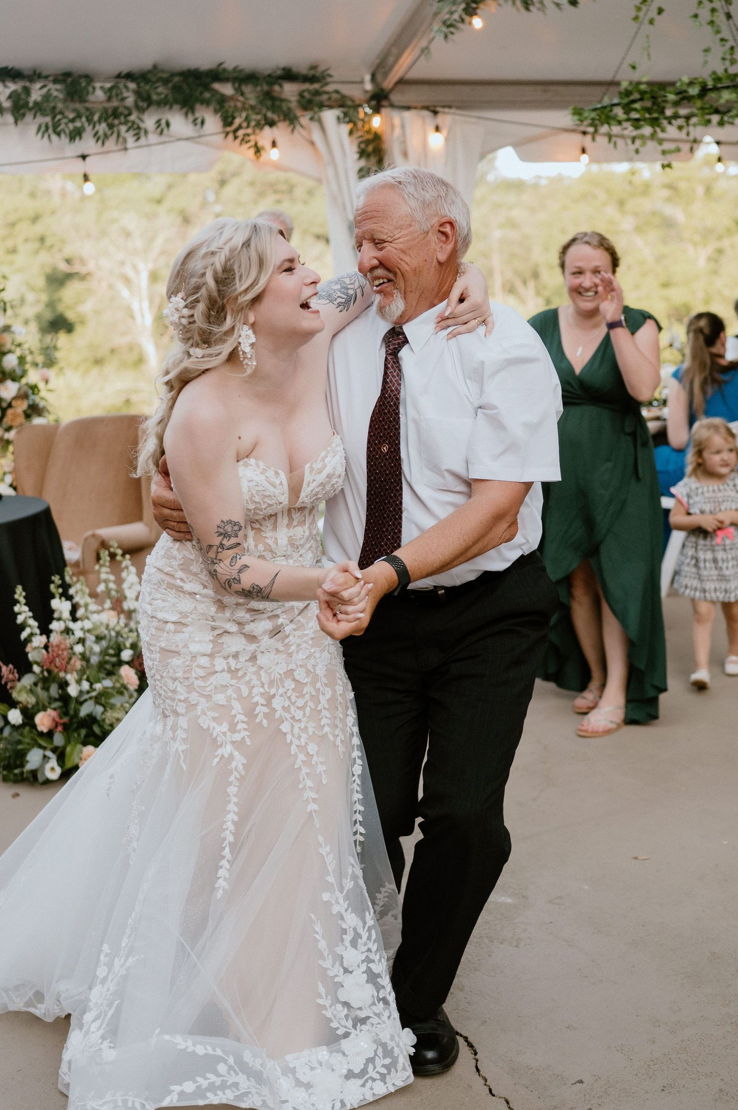 Joyful dance moment during wedding reception under tent with string lights and greenery.