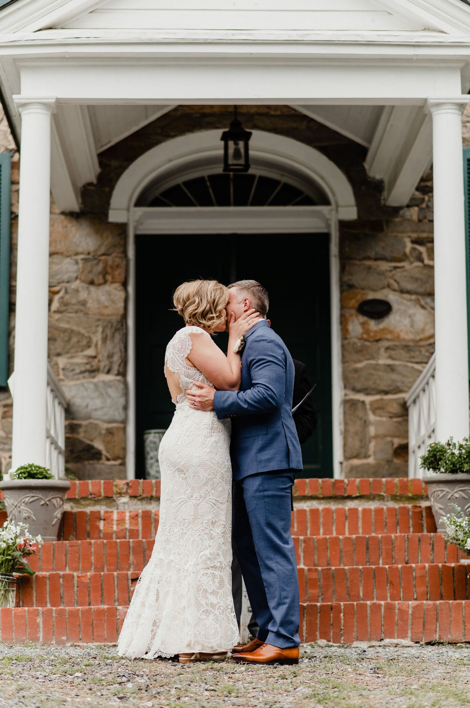A couple shares their first kiss on brick steps beneath an elegant stone archway with a fanlight window.